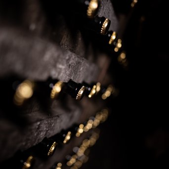 Dunkle Detailaufnahme von Sekt-Flaschen im Holzregal im Geldermann-Weinkeller