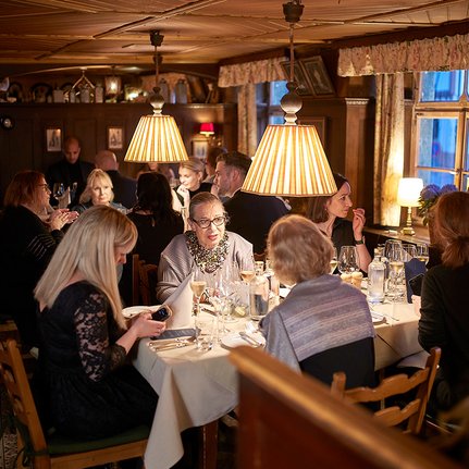 Eine Gruppe von Gästen sitzt an einem festlich gedeckten Tisch in einem gemütlichen Restaurant, umgeben von warmem Licht.