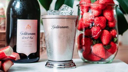 Der silberne Geldermann-Becher mit Eiswürfeln wird von einer Flasche Sekt und einem Glas voller saftiger Erdbeeren umgeben.