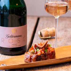 Auf einem Holzbrett liegt eine appetitliche Bruschetta, garniert mit frischen Zutaten, begleitet von einem Glas Rosé.