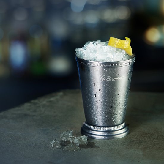 Auf einem dunklen Tisch steht ein kühler Becher mit Eis und einer gelben Zitronenscheibe, der eine erfrischende Atmosphäre vermittelt.