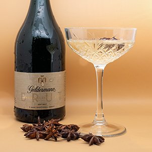 Ein Glas mit schimmerndem Sekt und Sternanis steht neben einer Flasche Geldermann, alles vor einem warmen, goldenen Hintergrund.