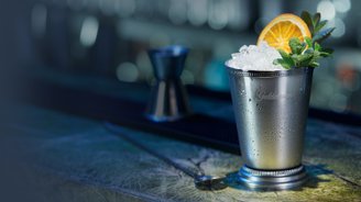 Der glänzende Becher, beschlagen mit Wassertropfen, enthält Eis und wird von einer Orangenscheibe und Minze dekoriert.