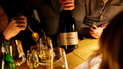 Die Szene zeigt eine Flasche Geldermann Sekt und mehrere Gläser, während eine Hand mit einem goldenen Löffel in der Nähe ist.
