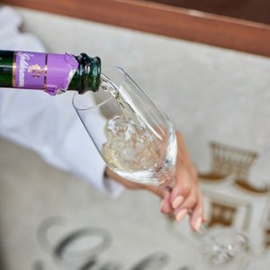 Ein Glas wird mit sprudelndem Sekt gefüllt, während eine Hand die Flasche mit lila Etikett hält.