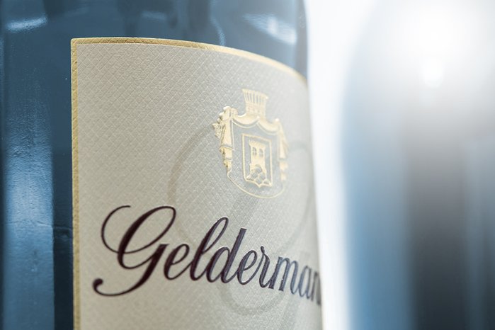 Ein elegantes Flaschenetikett mit dem Namen 'Gelderman', verziert mit goldenen Akzenten und einem Wappen im Hintergrund.