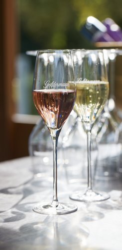Ein elegantes Glas mit roséfarbenem Sekt steht im Vordergrund, während ein weiteres Glas mit weißem Sekt im Hintergrund sichtbar ist.