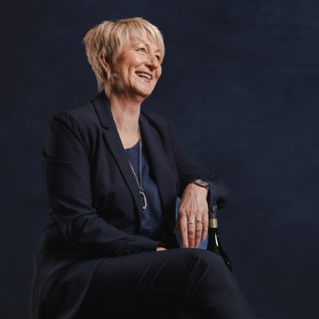 Sieglinde Schütz in dunkelblauem Anzug, fotografiert auf einem Hocker vor dunkelblauer Wand