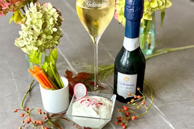 Ein elegantes Arrangement mit einem Glas Sekt, einer Flasche Sekt und frischen Gemüsesticks auf einem grauen Tisch.