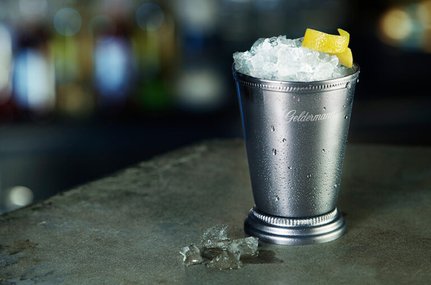 Ein eleganter Metallbecher gefüllt mit Eis und einem Zitronenschnitz, auf einer glatten Oberfläche platziert.