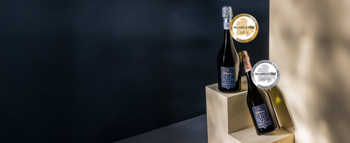 Die Flaschen Crémant sind mit Auszeichnungen versehen und stehen auf einem minimalistischen Podest vor einem dunklen Hintergrund.