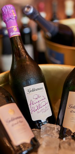 Drei Flaschen Geldermann Sekt stehen in einem Eiskübel, umgeben von Eiswürfeln und weiteren Flaschen im Hintergrund.