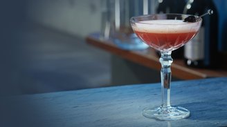 Ein eleganter Cocktail in einem Kristallglas steht auf einer blauen Theke, im Hintergrund sind Flaschen sichtbar.