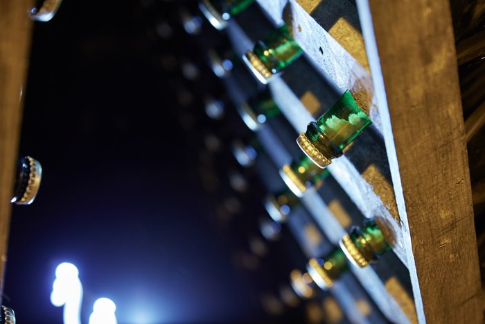 Grüne Flaschen sind ordentlich auf einem Holzgestell platziert, während ein schwaches Licht die Szene erhellt.