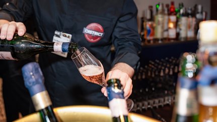Ein Barkeeper schenkt sprudelnden Rosé in ein elegantes Glas, während Flaschen im Hintergrund sichtbar sind.