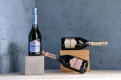 Ein stilvolles Arrangement von Sektflaschen in verschiedenen Farben, vor einer strukturierten blauen Wand, strahlt Eleganz aus.