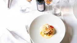 Ein weißer Teller mit liebevoll angerichteten Hummer mit Papayasalat auf einer weißen Tischdecke