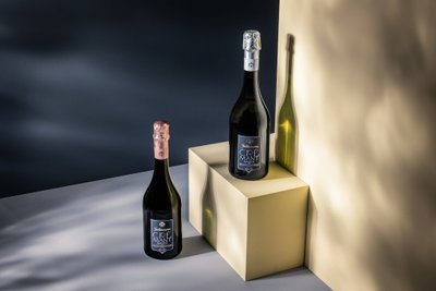Zwei Flaschen Crémant stehen auf einem hellen Würfel, beleuchtet von sanften Schatten und einem dunklen Hintergrund.