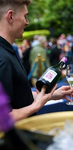 Ein junger Mann schenkt die Bayreuther Festspiel Cuvée 2025 in ein Sektglas ein.