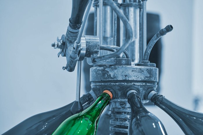 Eine grüne Flasche wird an einer industriellen Abfüllmaschine positioniert, um mit einem Korken verschlossen zu werden.