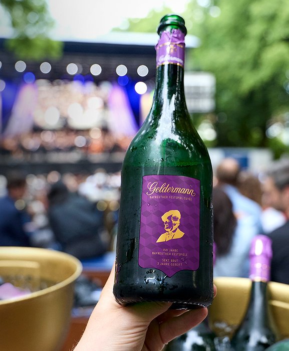 Eine Flasche der Geldermann Bayreuther Festspiel Cuvée 2026 vor dem Hintergrund der Festspielwiese