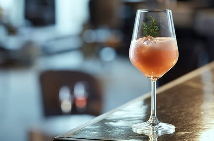 Weinglas mit lachsfarbenem Cocktail, garniert mit Thymian und Eiswürfeln auf einer Theke.