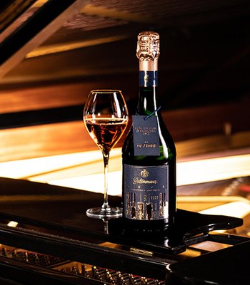 Eine elegante Flasche Sekt steht neben einem Glas auf einem Klavier, umgeben von warmem Licht und luxuriösem Ambiente.