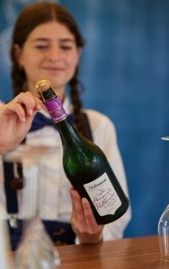 Eine junge Frau mit Zöpfen hält eine Sektflasche und lächelt, während sie den Korken öffnet.
