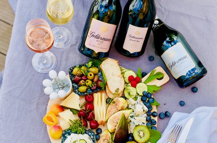 Ein üppiges Käse- und Obstbrett mit frischen Beeren, Trauben und verschiedenen Käsesorten, umgeben von drei Flaschen Sekt.