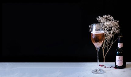 Ein elegantes Glas mit roséfarbenem Getränk steht auf einem Tisch, umgeben von zarten, trockenen Blumen und einer Flasche.