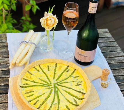 Ein appetitlicher Spargelkuchen mit einer goldenen Kruste, begleitet von einer Flasche Sekt und einem Glas Roséwein.