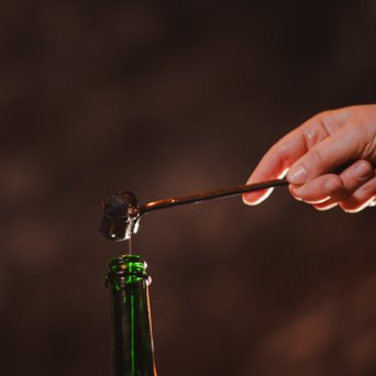 Eine Hand mit einem Löffel, der eine tropfende Flüssigkeit über einer Flasche hält, erzeugt eine spannende Momentaufnahme.