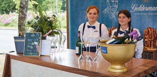 Der Getränkestand bietet Sekt und Gläser, während die beiden freundlichen Servicemitarbeiterinnen lächeln und bereit sind zu bedienen.