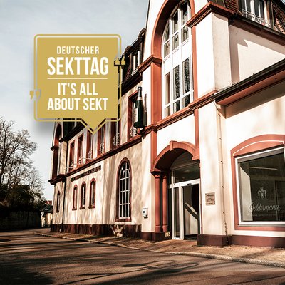 Die Fassade eines eleganten Gebäudes mit großen Fenstern und einem Sektflaschen-Symbol, das den Deutschen Sekttag bewirbt.