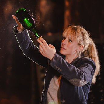 Eine Frau hält eine grüne Flasche in der Hand und betrachtet sie aufmerksam, während sie in einem dunklen Raum steht.