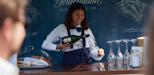 Eine fröhliche Kellnerin in eleganter Kleidung schenkt Sekt in ein Glas an einem stilvollen Stand aus.