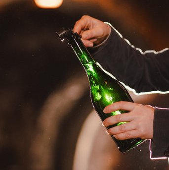 Eine Person hält eine grüne Flasche und öffnet sie vorsichtig, während Lichtstrahlen im Hintergrund schimmern.