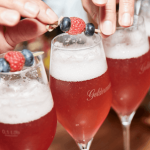 Ein fruchtiger Cocktail in einem eleganten Glas, garniert mit frischen Beeren, während jemand eine Beeren-Spieß hinzufügt.