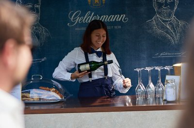 Eine fröhliche Kellnerin in eleganter Kleidung schenkt Sekt in ein Glas an einem stilvollen Stand aus.