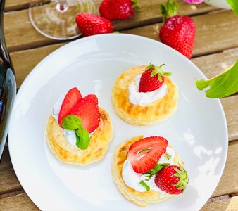 Drei knusprige Blätterteig-Törtchen auf einem weißen Teller, garniert mit frischen Erdbeeren und einem Klecks Sahne.