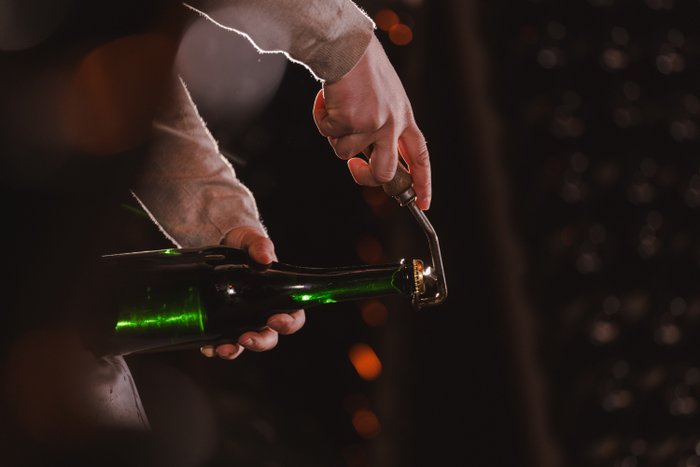 Eine Hand hält eine grüne Flasche, während ein Korkenzieher den Korken vorsichtig entfernt, um den Inhalt freizugeben.