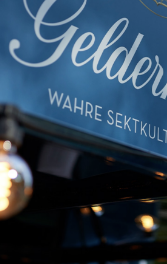Das Schild von Geldermann hebt sich vor einem blauen Hintergrund hervor, umgeben von warmen Glühbirnen, die eine einladende Atmosphäre schaffen.
