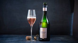 Ein elegantes Glas mit roséfarbenem Sekt steht neben einer Flasche Geldermann Grand Rosé auf einem dunklen Tisch.