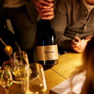 Ein festlicher Tisch mit einer Geldermann Sektflasche im Mittelpunkt, während eine Hand die Flasche öffnet und andere Gäste beobachten.