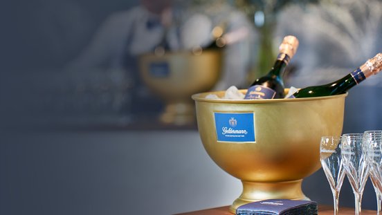 Ein eleganter goldener Sektkühler mit Flaschen und Eis, umgeben von Gläsern auf einem stilvollen Tisch.