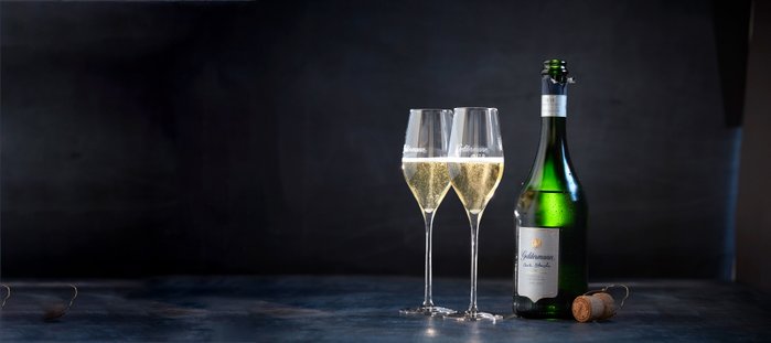 Zwei elegante Sektgläser stehen neben einer Flasche Sekt auf einem dunklen Tisch, bereit für einen festlichen Anlass.