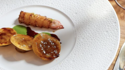 Ein stilvoll angerichtetes Gericht mit einer Garnele, goldbraunen Teigstücken und einer grünen Sauce auf einem eleganten Teller.