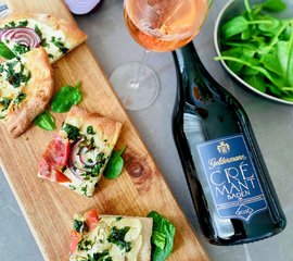 Ein Glas Roséwein steht neben einer Flasche Crémant und köstlichen Flammkuchenstücken auf einem Holzbrett.