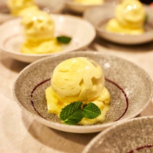 Ein Dessertteller mit einer gelben Eiskugel, umgeben von weiteren Tellern mit ähnlichen Leckereien im Hintergrund.