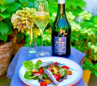 Ein frischer Salat mit Sardinen, serviert auf einem Teller, umgeben von üppigem Grün und einer Flasche Crémant.